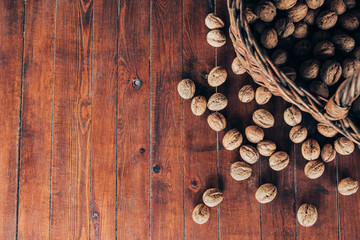 Fototapeta na wymiar Whole walnuts background. Whole walnuts scattered on an old wooden table near a wicker basket, background with place for inscription