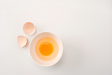 Beautyful brown chicken egg is half broken with yolk. Raw uncooked egg in white bowl on white kitchen table background.