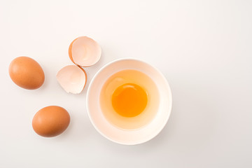 Beautyful brown chicken eggs and half broken with yolk. Raw uncooked egg in white bowl on white kitchen table background.