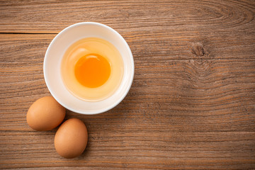 Fesh raw brown chicken eggs and Beautyful brown chicken egg is half broken with yolk. Raw uncooked egg in white bowl. Wooden kitchen table background.