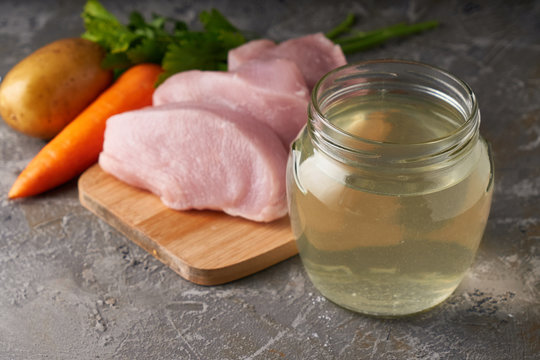 fresh poultry broth in a glass jar on a table with vegetables and pieces of fresh poultry meat