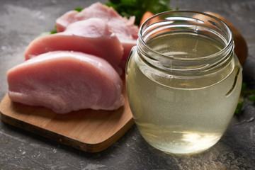 fresh poultry broth in a glass jar on a table with vegetables and pieces of fresh poultry meat