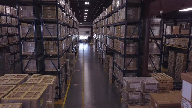Forward aerial shot of boxes stacked tall in industrial warehouse