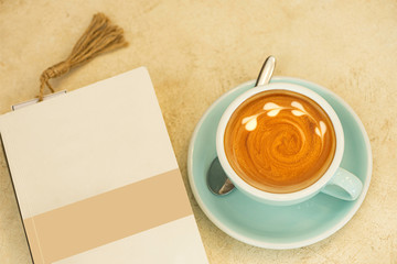 A blank book placed on the table to read with the hot capucino with the copy space.