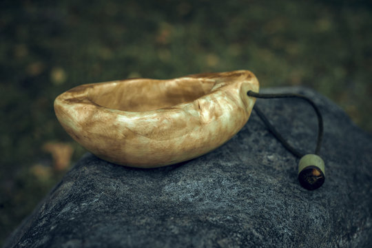 A wooden mug made of suvel Karelian birch stands on a stone in the forest.