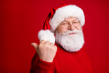 Photo of old man in santa claus headwear point thumb finger copyspace demonstrate fairy magic newyear discounts wear trendy x-mas sweater jumper isolated bright shine color background