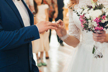 bride puts a gold wedding ring on the finger of the groom