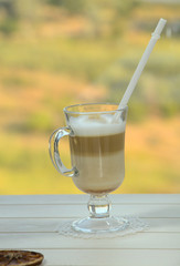 Latte on a background of green meadow from the window. Hot drink for breakfast. Romantic morning with a cup of coffee, with a beautiful view from the window.