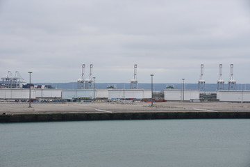 Obraz premium Empty Le Havre Port in France with uplifted gantry cranes without movement due to reduced traffic in the port caused by coronavirus, COVID-19 and general lockdown during overcast bad weather.