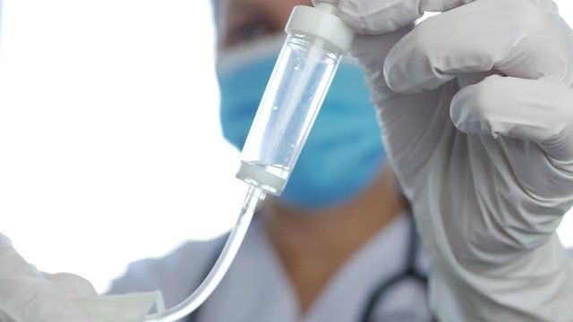Blurred Image with a Doctor Wearing Protective Mask and Surgery Gloves in Emergency Hospital Room Checking Intravenous Perfusion