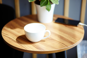 Empty white cup and smart phone on table in cafe. Morning light falls from the window.Coffee break.Blurred image,selective focus