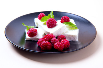 Ice cream with raspberries and mint on a black plate, white background