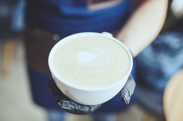 Barista wearing medical latex black gloves, making cappuccino, bartender preparing coffee drink. Blurred image, selective focus