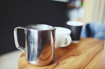 Blurred image of milk jug and a cup of coffee on wooden table in cafe. Coffee break  