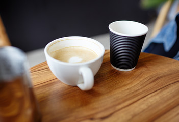 White cup coffee and disposable paper cup on wooden table in cafe. Coffee break. Blurred image,selective focus