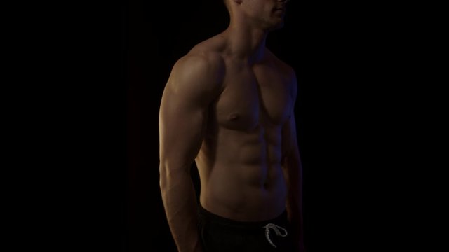 Young fit man on black background. Slowly zoom out. Artistic colored light