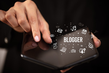 Businessman holding a foldable smartphone with BLOGGER inscription, social media concept