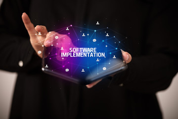 Businessman holding a foldable smartphone with SOFTWARE IMPLEMENTATION inscription, new technology concept