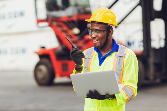 African American black worker working in logistic shipping cargo port site happy work control loading with radio and laptop.