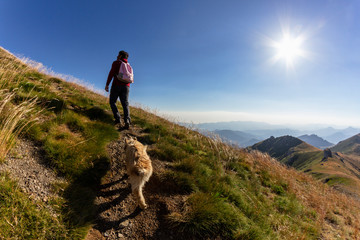 Naklejka na ściany i meble Man climbing to the top of a mountain Coriscao with a dog in Leon on a sunny day, Spain