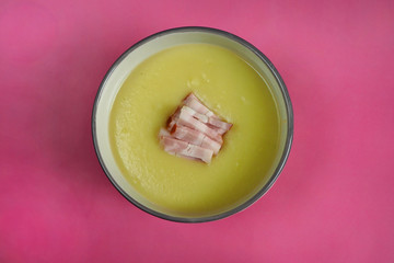grey plate with cream soup of zucchini, potatoes, cream, onions and bacon slices on a pink background top view . cooking food at home