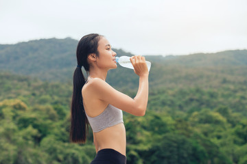  Girl in sportswear drinks water from recycled plastic bottle in park outdoors after Training