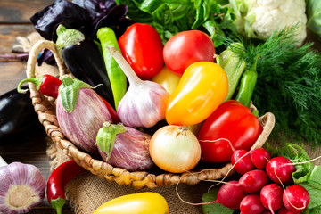 Assortment of vegetables in a basket on the table. A lot of different raw vegetables in the basket. Eggplant, tomatoes, garlic, sweet pepper, onion on the table. The concept of healthy eating