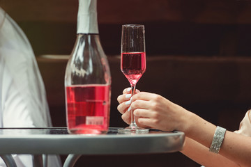 Young Girl hand holding a glass with pink champagne. Open bottle on a table