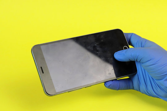 Hand In A Medical Glove And Dirt On The Surface Of A Smartphone. Copy Space - Equipment Cleaning Concept, Cleanliness, Spread Of Coronavirus, Prevention, Bacteria Elimination