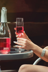 Young Girl hand holding a glass with pink champagne. Open bottle on a table
