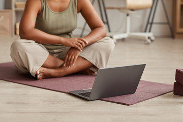 Naklejka premium Close-up of woman sitting on exercise mat in front of laptop and watching yoga exercises online at home