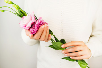 Beautiful purple eustoma flower in young woman's hands with nude manicure. Lady in white sweater. Soft focus closeup. Pink blooming spring fresh plant. Elegant feminine floral background