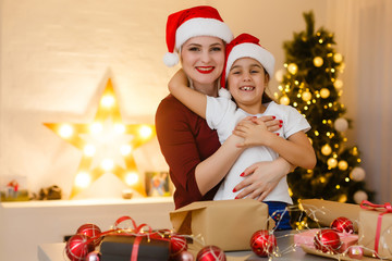 Cheerful pretty mother and her adorable little daughter enjoying beauty of handmade Christmas decoration while sitting at desk, interior of cozy living room on background