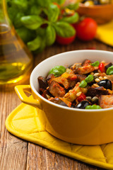 Traditional Italian caponata, served with croutons in a yellow, sunny pot. Decorated with basil and pine nuts.