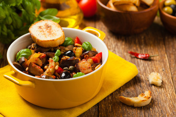 Traditional Italian caponata, served with croutons in a yellow, sunny pot. Decorated with basil and...