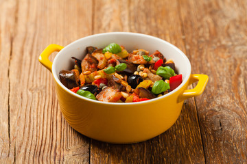 Traditional Italian caponata, served with croutons in a yellow, sunny pot. Decorated with basil and pine nuts.