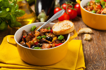 Traditional Italian caponata, served with croutons in a yellow, sunny pot. Decorated with basil and pine nuts.