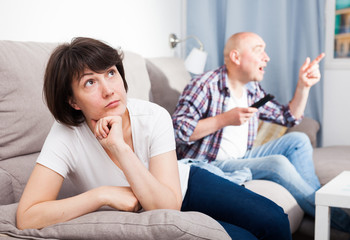 Obraz na płótnie Canvas Sad woman sitting on the sofa. Next to her husband watching TV. High quality photo