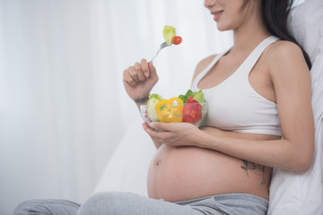 care about unborn child. pregnancy, healthy food and people concept, happy pregnant woman eating vegetable salad for breakfast sitting on bed at home. pregnancy and healthy organic nutrition.