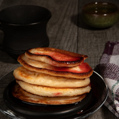 Several pancakes with cherry jam on wood background