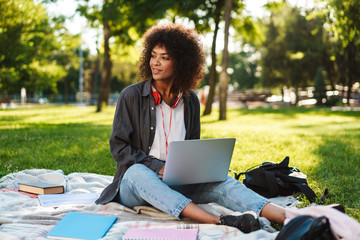 Image of african american girl smiling and doing homework with laptop