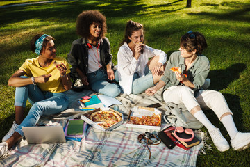 Image of funny nice student girls eating pizza while doing homework