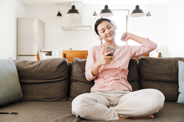 Smiling asian woman on couch listening to music at home