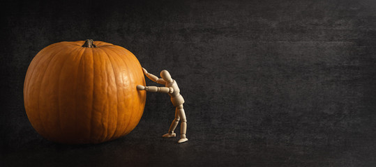 Wooden human miniature rolling pumpkin on black background. Halloween coming soon. Copy space