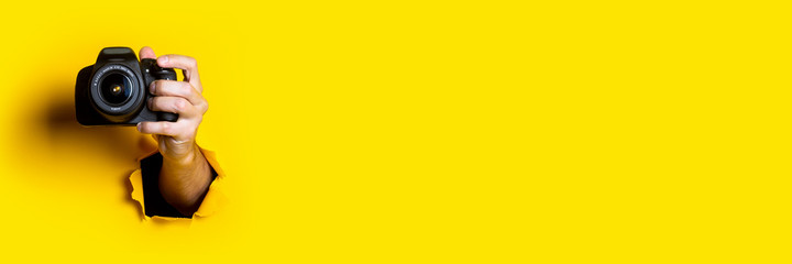 Man's hand holding a camera on a bright yellow background. Banner.