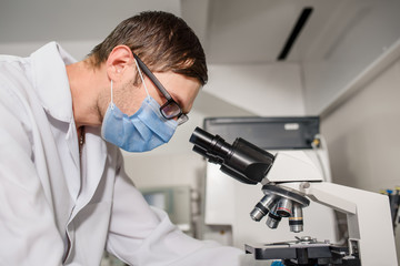 In the hospital laboratories working process, a young man doctor is looking in the medical microscope