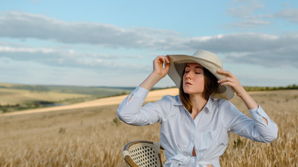 Young woman in white shirt and hat is in the wheat field.