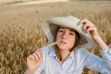 Woman in white shirt and hat is holding a bunch of wheat in the wheat field.