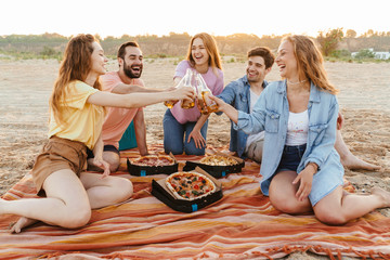 Image of young happy people laughing and drinking beer by seaside