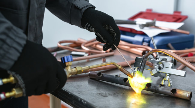 Worker is soldering a pipe by a blow lamp on a factory workbench background. Pipework.